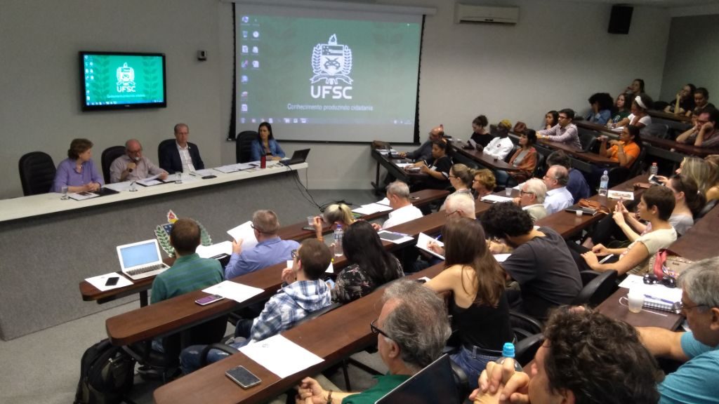 Foto dos conselheiros do Conselho Universitário sentados ouvindo o reitor na sala dos conselhos.